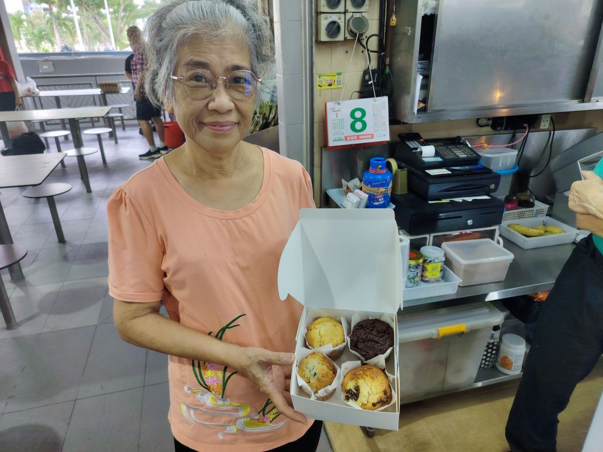 Christina, co-owner of Bakes n Bites, holding a box of freshly baked muffins